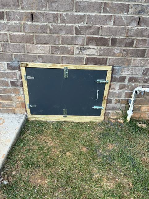 New black crawl space access door in a brick foundation wall