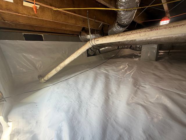 White crawl space liner running along plumbing and ductwork